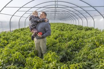 Ukrainian father and child stand in a greenhouse among growing plants.