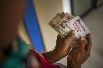 Image: Hands holding cash and a Prosper Global ID card during a distribution of emergency cash