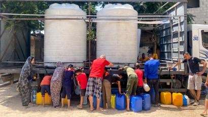 Palestinians filling jerrycans from water tender truck.